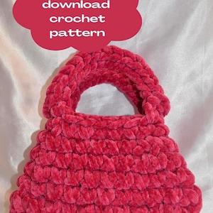 Puede incluir: Un bolso de ganchillo hecho a mano, de felpa, color frambuesa, con un asa redondeada. La superficie texturizada del bolso está hecha de un hilo suave y aterciopelado. Un gráfico rojo en forma de nube dice "Digital download crochet pattern".