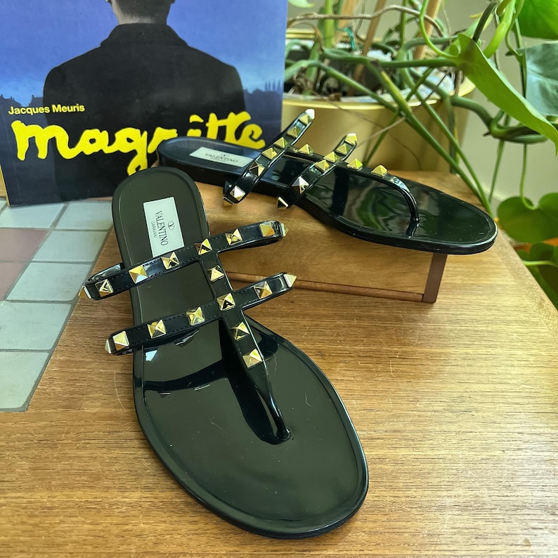 Y2K Valentino Garavani Rockstud Jelly Sandals - Black PVC Thong Flip Flops - Women's Size 40 US 10 - Studded Shoes Made in Italy

Edgy sophistication to your summer wardrobe!
Valentino Garavani Rockstud Jelly Sandals. A cult favorite in the Valentino lineup, these sandals combine the effortless ease of a jelly flip-flop with the high- fashion impact of the iconic pyramid Rockstuds.

Premium high-shine black PVC, these sandals feature the
signature silver-tone studs along the straps.