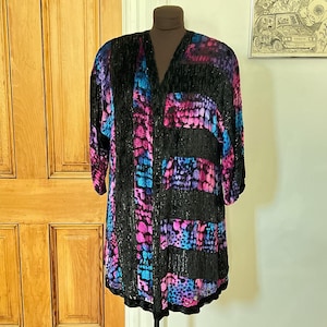 May include: A long-sleeved, button-down garment with a V-neck, featuring a black base with horizontal black stripes. The garment is adorned with a vibrant pattern of pink, blue, and purple spots. The hemline is trimmed with black lace.
