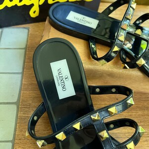Y2K Valentino Garavani Rockstud Jelly Sandals - Black PVC Thong Flip Flops - Women's Size 40 US 10 - Studded Shoes Made in Italy

Edgy sophistication to your summer wardrobe!
Valentino Garavani Rockstud Jelly Sandals. A cult favorite in the Valentino lineup, these sandals combine the effortless ease of a jelly flip-flop with the high- fashion impact of the iconic pyramid Rockstuds.

Premium high-shine black PVC, these sandals feature the
signature silver-tone studs along the straps.