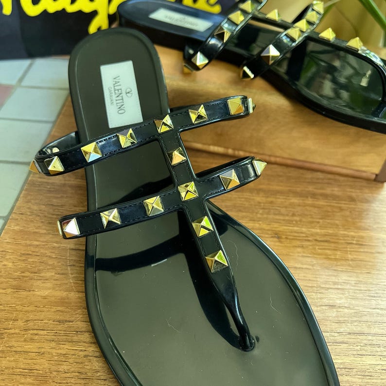 Y2K Valentino Garavani Rockstud Jelly Sandals - Black PVC Thong Flip Flops - Women's Size 40 US 10 - Studded Shoes Made in Italy

Edgy sophistication to your summer wardrobe!
Valentino Garavani Rockstud Jelly Sandals. A cult favorite in the Valentino lineup, these sandals combine the effortless ease of a jelly flip-flop with the high- fashion impact of the iconic pyramid Rockstuds.

Premium high-shine black PVC, these sandals feature the
signature silver-tone studs along the straps.