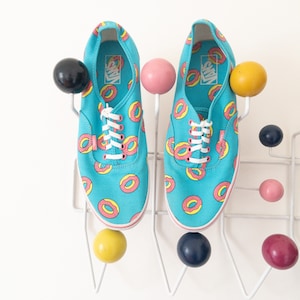 May include: A pair of blue canvas sneakers with a donut pattern. The sneakers have white laces and are hanging on a white rack with colorful hooks.