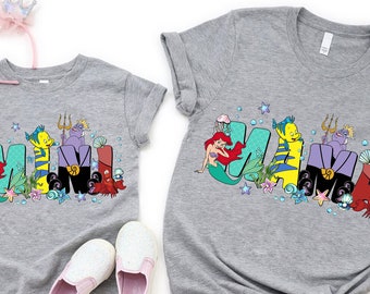 May include: Two gray t-shirts with the word "MAMA" and "MINI" spelled out in colorful cartoon characters from the Little Mermaid. The characters include Ariel, Flounder, Ursula, and Sebastian.