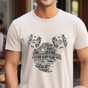 May include: A white t-shirt with a gray graphic of the Death Star from Star Wars, designed to look like Mickey Mouse ears. The text "Soft Cream" is printed in the bottom right corner of the shirt.