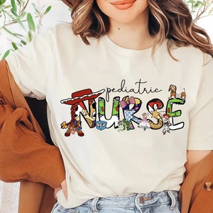 May include: White t-shirt with a graphic of the word "NURSE" made up of characters from the Toy Story movie franchise. The word "pediatric" is written above the graphic.