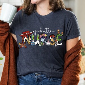 May include: A navy blue t-shirt with a white graphic of the word "pediatric" and the word "NURSE" spelled out with characters from the Toy Story franchise.