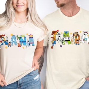 May include: Two cream-colored t-shirts with the words "NANA" and "PAPA" in blue letters. The letters are decorated with characters from the movie Toy Story. The shirts are worn by two people.