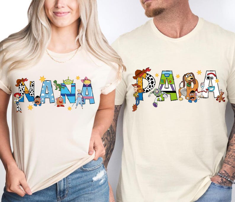 May include: Two cream-colored t-shirts with the words "NANA" and "PAPA" in blue letters. The letters are decorated with characters from the movie Toy Story. The shirts are worn by two people.