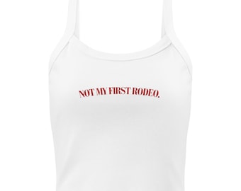 May include: White crop top with spaghetti straps. The text "NOT MY FIRST RODEO." is printed in red across the front. The top is made of a soft, lightweight material.