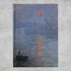 Puede incluir: Cuaderno con una reproducción de una pintura que representa una escena portuaria al atardecer. La obra de arte muestra un sol rojo, un barco con figuras y reflejos en el agua. La paleta de colores está dominada por azules, naranjas y grises.