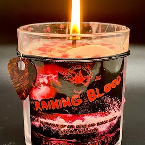 May include: A red and black candle with a label that reads "RAINING BLOOD" and "A downpour of red wine and black cherry inspired by Slayer. The sky is turning red."
