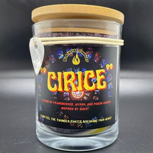 May include: A black glass candle jar with a wooden lid. The label features a stained glass design and the text "CIRICE", "A HYMN OF FRANKINCENSE, MYRRH, AND POISON CROCUS", "INSPIRED BY GHOST", and "I CAN FEEL THE THUNDER THAT'S BREAKING YOUR HEART".