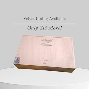 Op de afbeelding: Een lichtgekleurde houten kist met de tekst "Davidoff MILLENNIUM ROBUSTO TUBOS" op de voorkant. De kist heeft een rechthoekige vorm en een scharnierend deksel. De tekst "Velvet Lining Available" staat boven de kist.