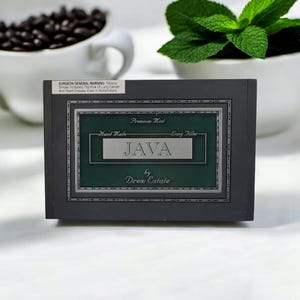 May include: A black box with a green label that reads "Premium Mint Hand Made - Long Filler JAVA by Drew Estate".