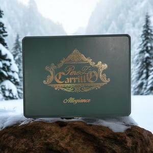 Peut inclure: Une boîte en bois verte avec un logo doré qui dit "Perez Carrillo" et le mot "Allegiance" en lettres dorées. La boîte est posée sur un rocher recouvert de neige.