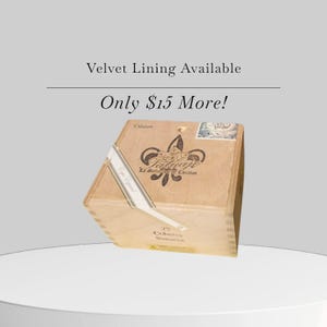 May include: A wooden box with a fleur-de-lis logo and the text "La Delicia de Casabor". The box has a white label with text and is labeled "25 Cohibas Nicaragua". The text "Velvet Lining Available" is above the box.
