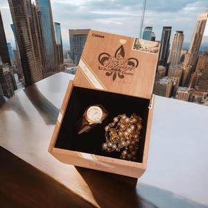 May include: A wooden box with a gold watch and a pearl necklace inside. The box is labelled "Cabinet", "La Deliciosa", and "Casador".