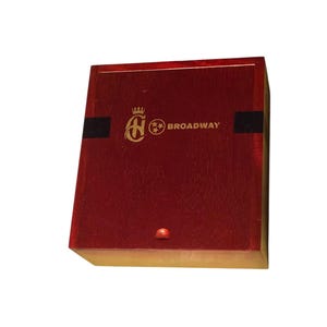 May include: A rectangular, wooden box with a deep red finish. The box features a gold emblem and the word "BROADWAY" in gold lettering. Two black stripes are on the front of the box.