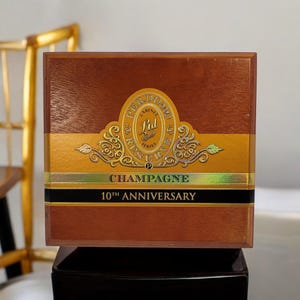 May include: A wooden box with a gold label that reads "Perdomo Cabinet Series Ltd. Reserve P Champagne 10th Anniversary".