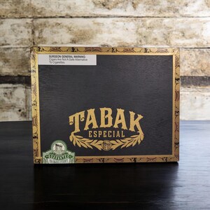 May include: A black wooden box with a gold label that says "TABAK ESPECIAL" and a green label that says "GUARANTEE". The box has a gold and black patterned border.