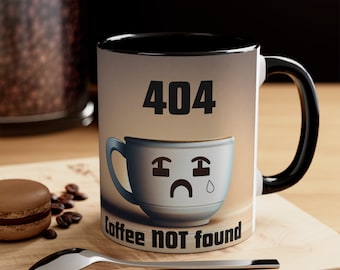 Könnte beinhalten: Eine weiße Kaffeetasse mit schwarzem Innenraum und Henkel. Die Tasse zeigt eine traurige Kaffeetassen-Grafik mit dem Text "404 coffee NOT found". Die Tasse steht auf einer Holzoberfläche mit einem Löffel und einem Macaron.