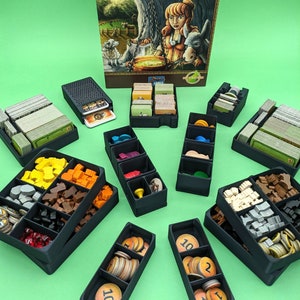May include: A Caverna: The Cave Farmers board game with multiple black plastic storage boxes filled with game pieces and cards. The boxes are organised by colour and type of game component. The game box is in the background.