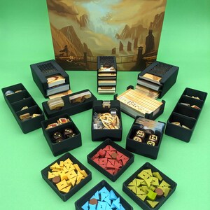 May include: A set of black plastic storage boxes for organizing game pieces. The boxes contain various colored plastic pieces, dice, and cards. The game box cover is visible in the background with the title "Near and Far" by Ryan Laukat.