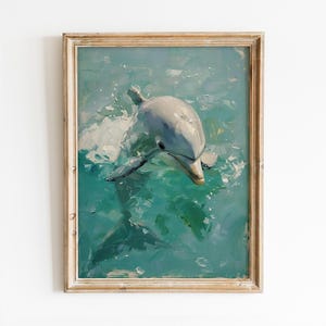Op de afbeelding: Een ingelijst schilderij van een dolfijn die in turquoise water zwemt. De dolfijn is grijs en wit, met zijn kop en rugvin zichtbaar. Het schilderij heeft een getextureerde, impressionistische stijl.