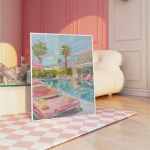 以下が含まれることがあります： ピンクのラウンジチェア、ヤシの木、バルコニーのある建物が描かれたリゾートプールのシーンを描いた額入りの絵画。アートワークは、白いフレームが付いたピンクと白のチェック柄のラグに表示されます。