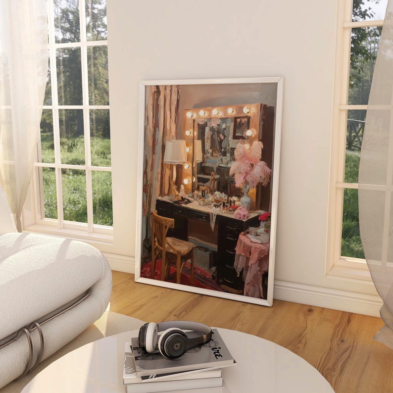 May include: A framed painting of a vanity with a lighted mirror, a wooden chair, and various beauty products. The painting is displayed in a room with large windows and a white sofa. A pair of headphones rests on a stack of books on a round table.