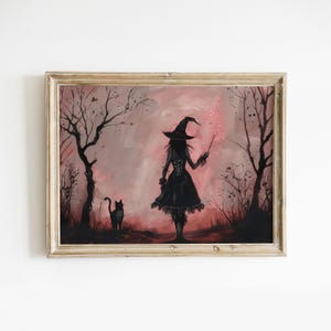 Op de afbeelding: Een ingelijst schilderij toont een heks in een zwarte jurk en hoed, met een toverstaf met roze glitters. Een zwarte kat staat in de buurt. De achtergrond is een roze en zwart landschap met bomen.