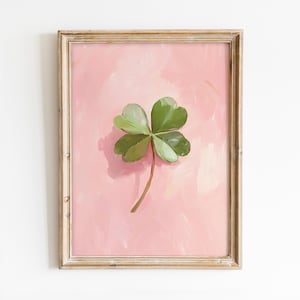 May include: A framed painting of a four-leaf clover on a pink background.