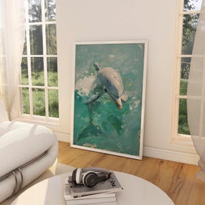Op de afbeelding: Een ingelijst kunstwerk met een dolfijn die in turquoise water zwemt. De dolfijn is geschilderd in grijstinten en wit, met een textuur. Het kunstwerk staat in een witte lijst, leunend tegen een witte muur.