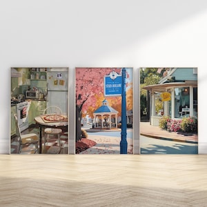May include: Three framed art prints depicting scenes from a town. One shows a kitchen with a pizza on a table. Another features a gazebo and a sign that reads "Stars Hollow". The third shows a storefront.