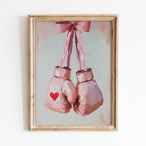 May include: A framed painting of two pink boxing gloves tied together with a pink ribbon. The gloves have a red heart painted on one of them.
