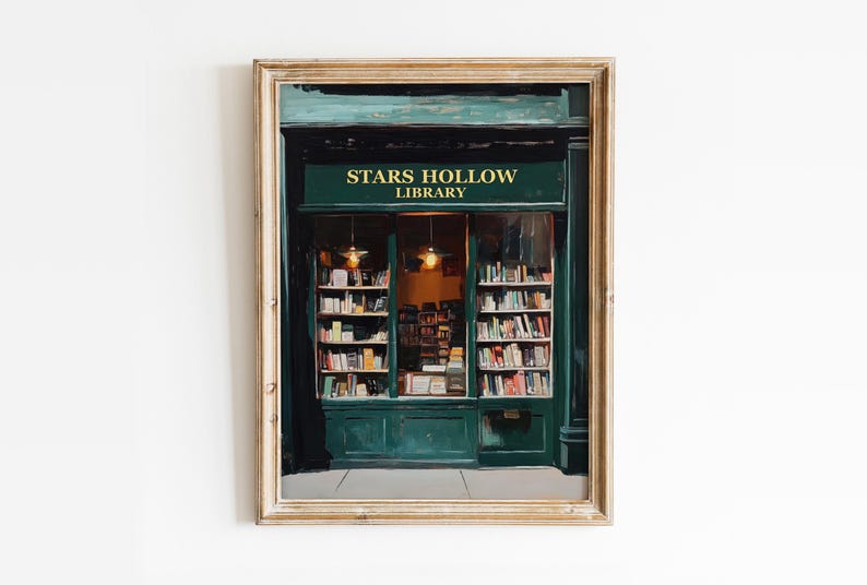 Op de afbeelding: Een ingelijste illustratie van een groene winkelgevel met de woorden "Stars Hollow Library" boven de ingang. De winkelgevel heeft grote ramen die boekenplanken vol boeken laten zien.