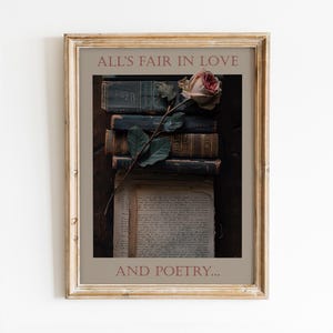 May include: Framed print featuring a stack of antique books with a rose and the text "ALL'S FAIR IN LOVE AND POETRY...". The books are dark with gold lettering, and the rose is a soft pink. The frame is a light gold color.