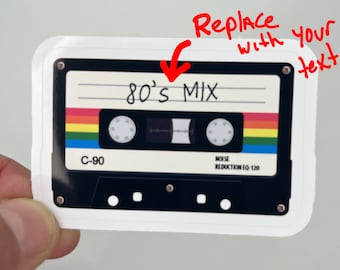 May include: A white cassette tape sticker with a black cassette tape design. The cassette tape has a rainbow colored stripe and the text "80's MIX" written on it.