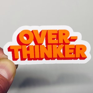 May include: White sticker with the text "OVER-THINKER" in orange and red letters. The letters are in a bold, blocky font.