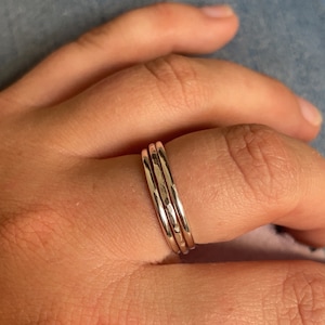 Pode incluir: Tr&ecirc;s an&eacute;is de prata empilh&aacute;veis em um dedo. Os an&eacute;is s&atilde;o finos e t&ecirc;m uma textura martelada.