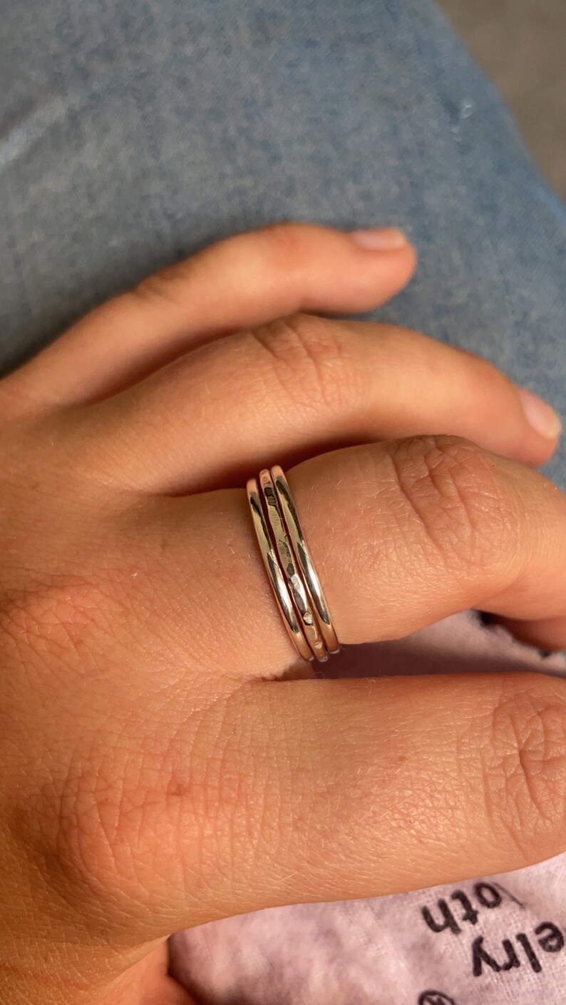 Pode incluir: Tr&ecirc;s an&eacute;is de prata empilh&aacute;veis em um dedo. Os an&eacute;is s&atilde;o finos e t&ecirc;m uma textura martelada.