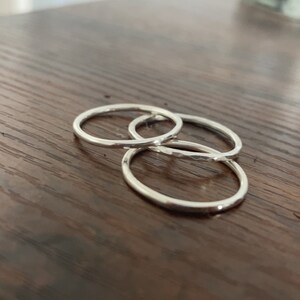 Pode incluir: Tr&ecirc;s an&eacute;is de prata empilhados uns sobre os outros em uma superf&iacute;cie de madeira.