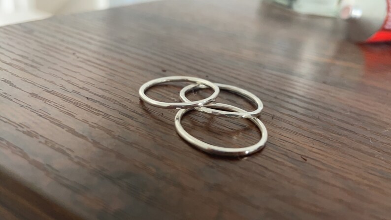 Pode incluir: Tr&ecirc;s an&eacute;is de prata empilhados uns sobre os outros em uma superf&iacute;cie de madeira.