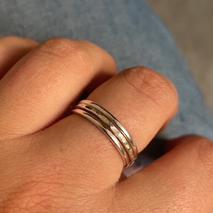 Pode incluir: Tr&ecirc;s an&eacute;is de prata empilhados em um dedo. Os an&eacute;is s&atilde;o finos e t&ecirc;m uma textura martelada.