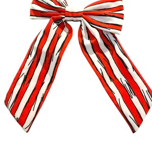 May include: A large, decorative bow with a red and white striped pattern. The bow features long, flowing tails and a central knot. The stripes are outlined in black, creating a bold contrast. This accessory is suitable for various occasions.