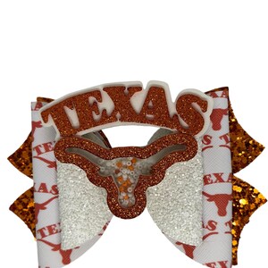May include: White and orange glitter bow with a white "TEXAS" cutout and a white and orange glitter Longhorn head cutout.