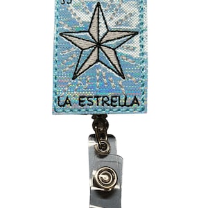 May include: A blue and silver badge holder with a white star and the text "LA ESTRELLA" on the front. The badge holder has a retractable clip.