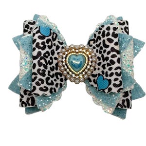 Puede incluir: Un lazo azul y blanco con estampado de leopardo con un corazón azul y un centro adornado con oro y perlas.