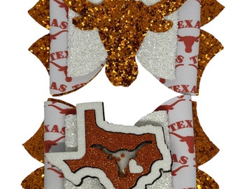 May include: Two hair bows with a white background and orange glitter. One bow features a silhouette of a longhorn steer head. The other bow features a silhouette of the state of Texas with a longhorn steer head inside. Both bows have the words "Texas" and "Longhorns" printed on them.