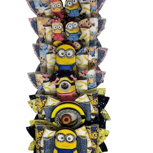 May include: A stack of five yellow and blue Minion character hair bows with glitter and denim accents. The bows are layered on top of each other and feature different Minion characters.
